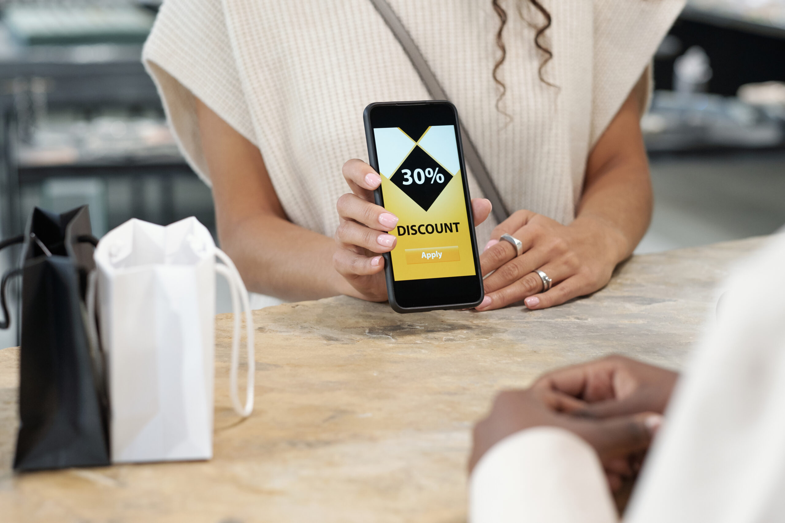 Vásárló digitális kupon és hűségprogram mobilalkalmazás használata közben egy üzlet pultjánál